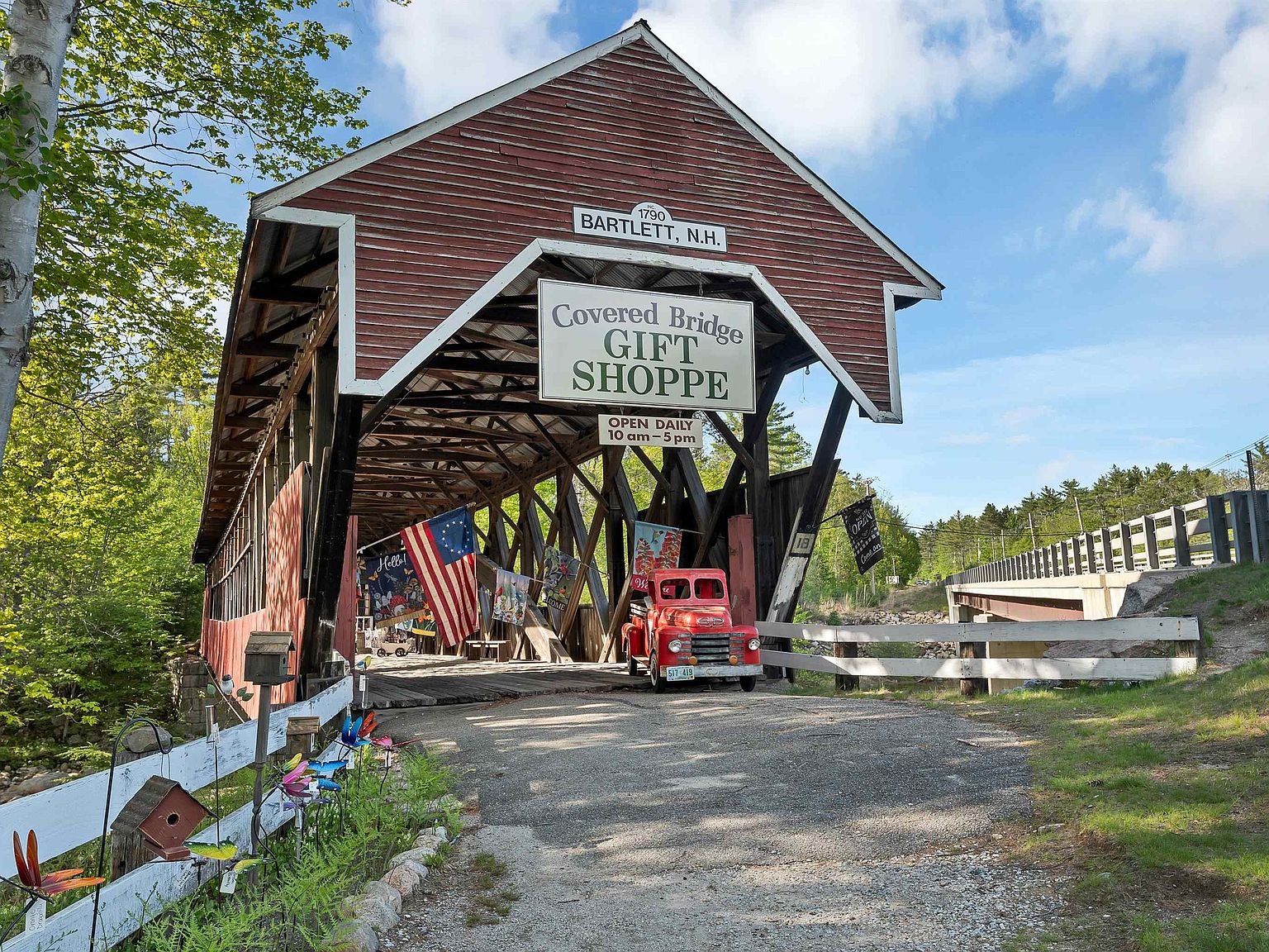 The bridge approached from the road, its red siding framing the Covered Bridge Gift Shoppe sign, with a vintage red service truck parked underneath